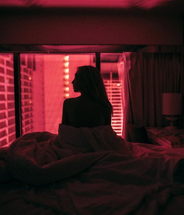 Woman in a calm, focused pose in a dark room with pink light accents.